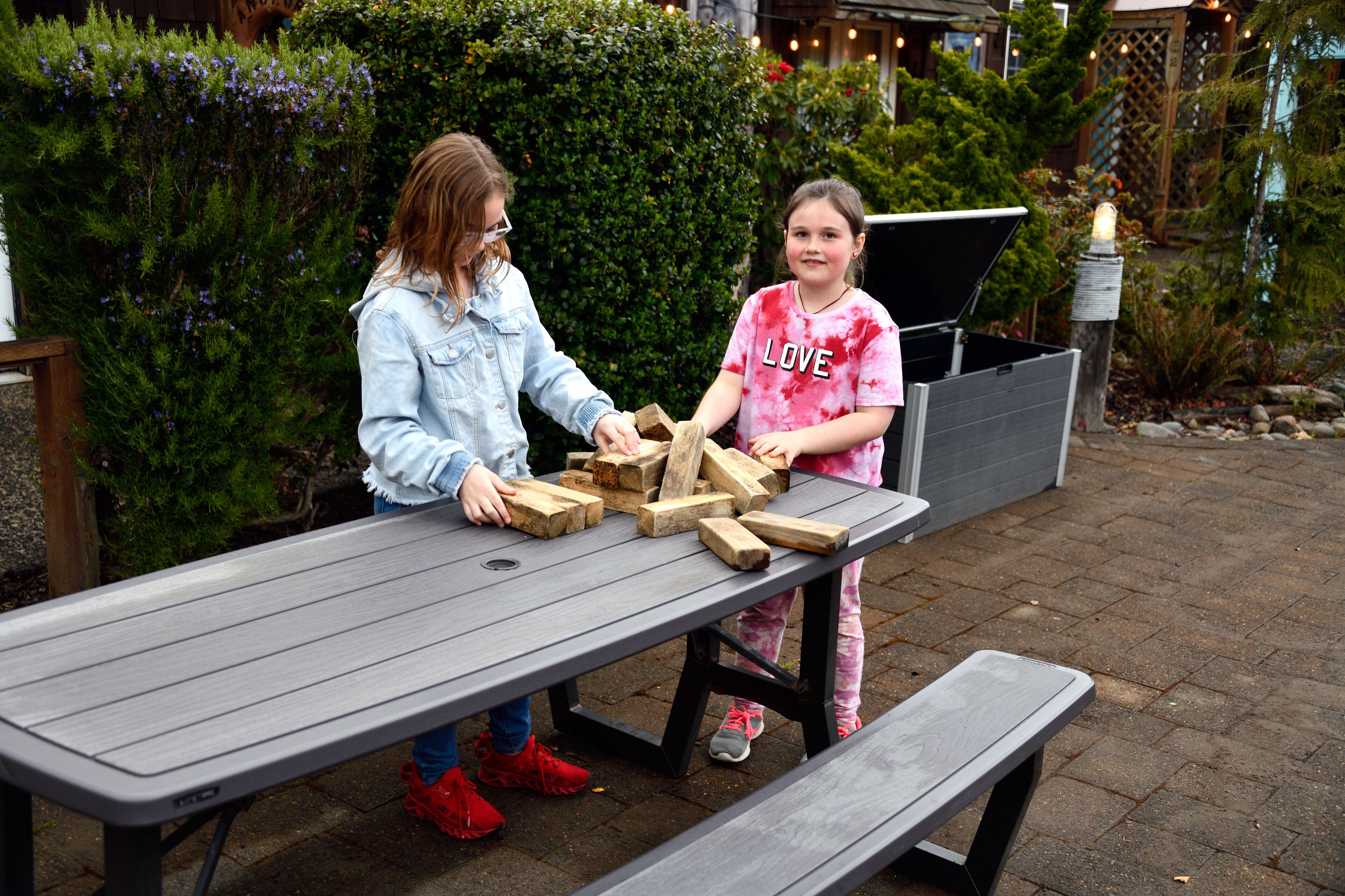 Two people playing with wooden blocks on a picnic table outdoors.
