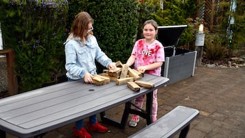 Two people playing with wooden blocks on a picnic table outdoors.