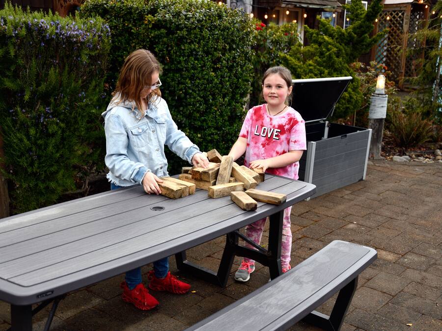 Two people playing with wooden blocks on a picnic table outdoors.