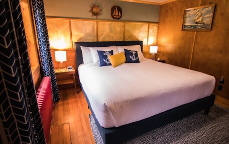 A neatly made bed with white and navy bedding, a wooden headboard, and two nightstands with lamps.