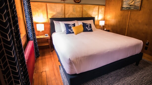 A neatly made bed with white and navy bedding, a wooden headboard, and two nightstands with lamps. - Anchor Inn Resort (Lincoln City)