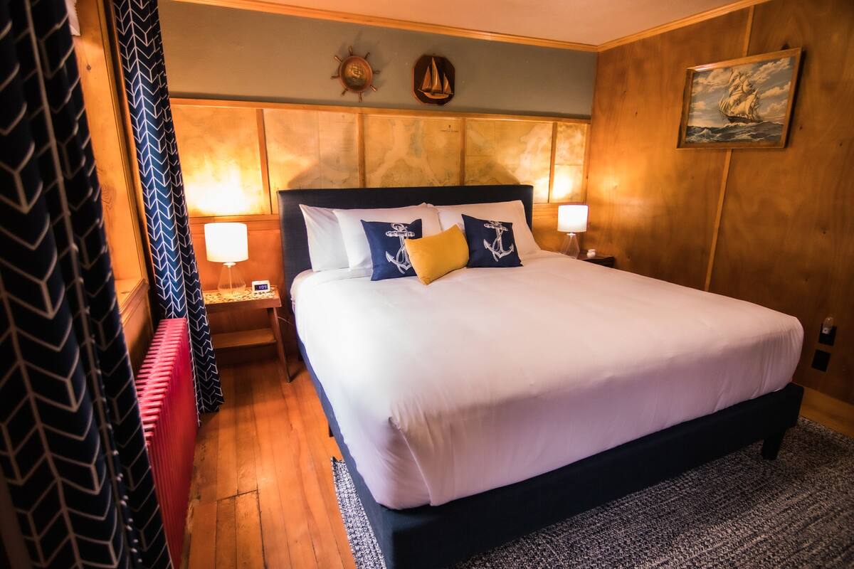 A neatly made bed with white and navy bedding, a wooden headboard, and two nightstands with lamps.