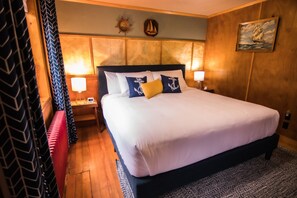 A neatly made bed with white and navy bedding, a wooden headboard, and two nightstands with lamps. - Anchor Inn Resort (Lincoln City)