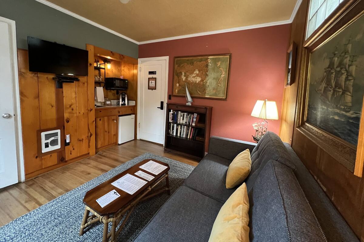 A living room with a sofa, a small coffee table, a bookshelf, a painting, and a television.