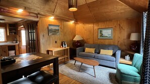 A cozy cabin interior with a wooden ceiling, a sofa, a coffee table, and a dining area with a table and chairs. - Anchor Inn Resort (Lincoln City)