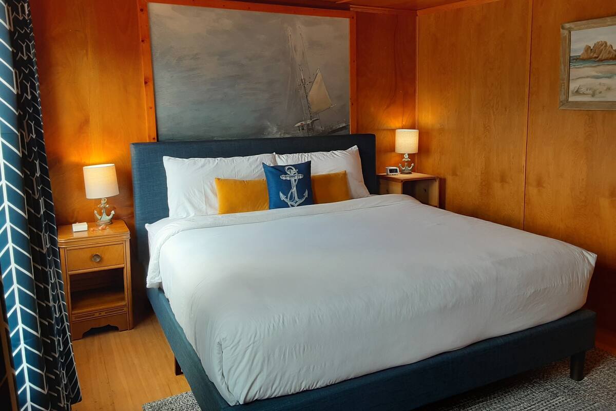 A neatly made bed with white linens and decorative pillows, a wooden headboard, and two bedside tables with lamps.