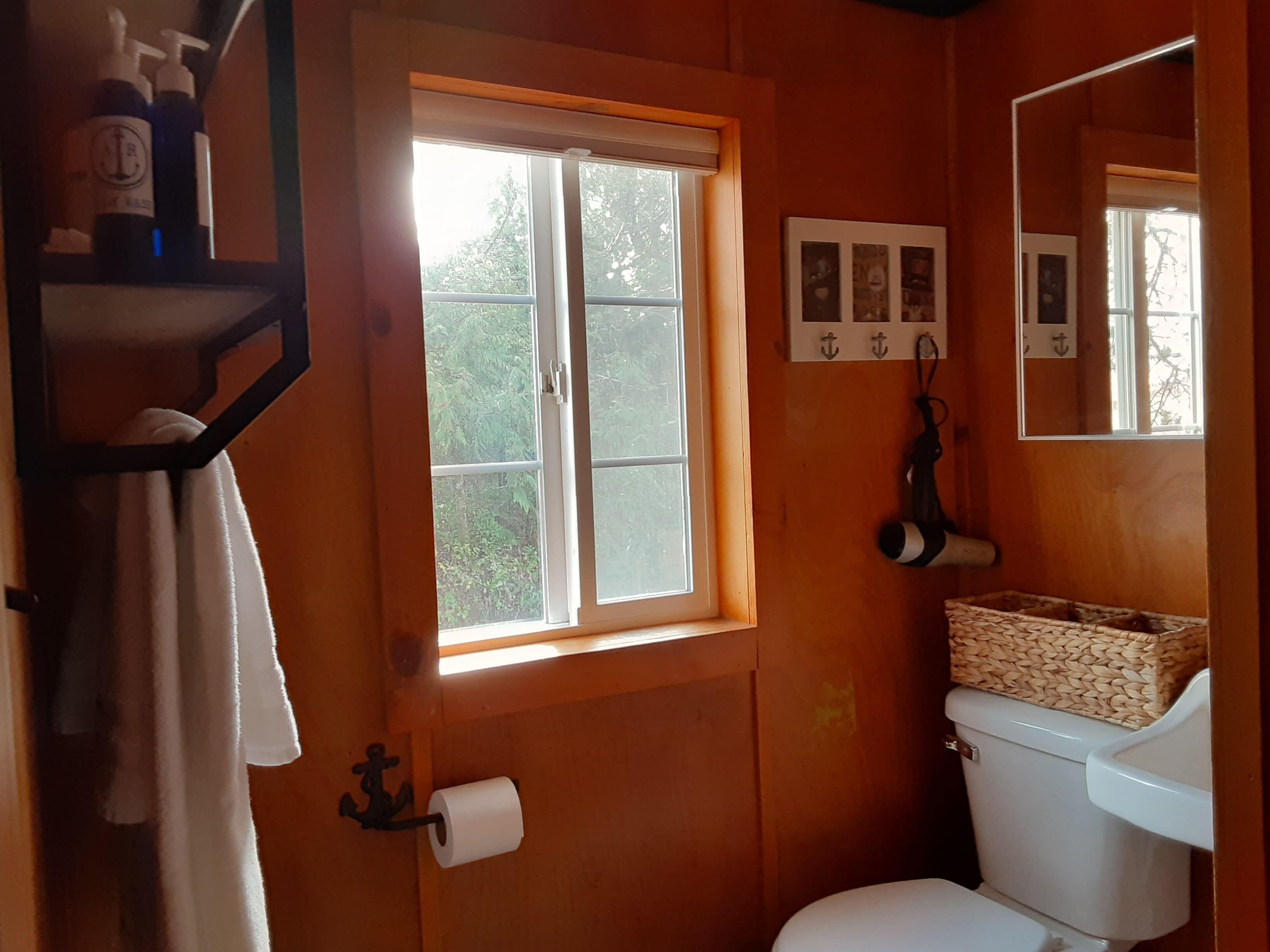 Et badeværelse med toilet, et vindue, et håndklædestativ og en hylde med toiletartikler.