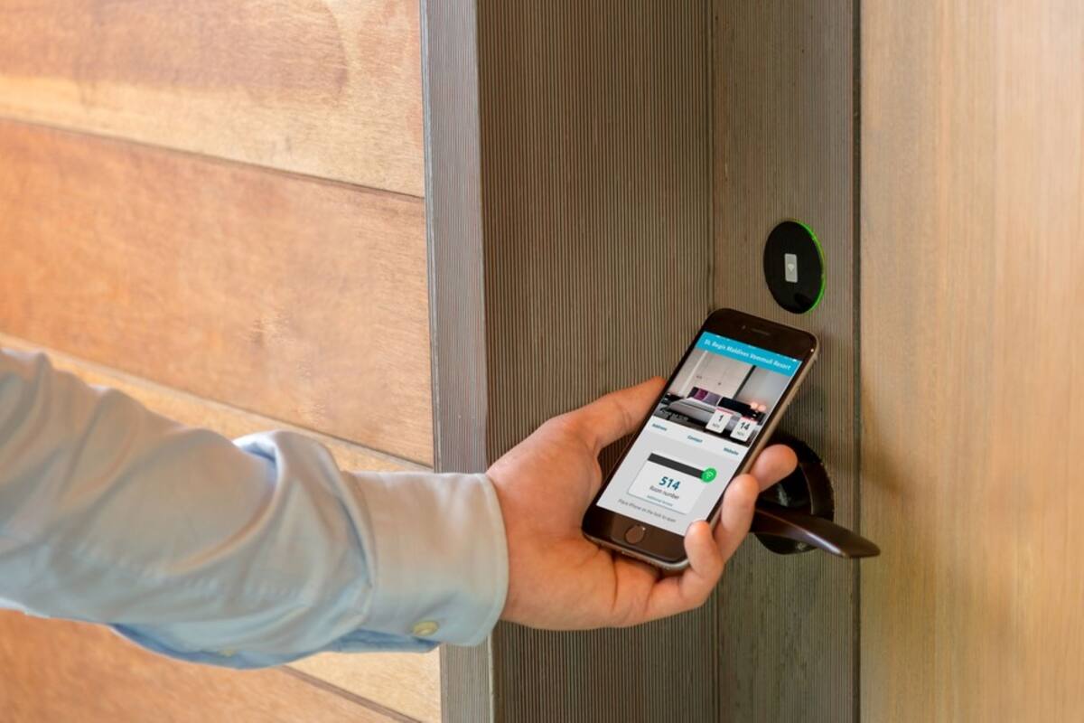 A person holding a smartphone near a door with a digital lock and a green indicator light.