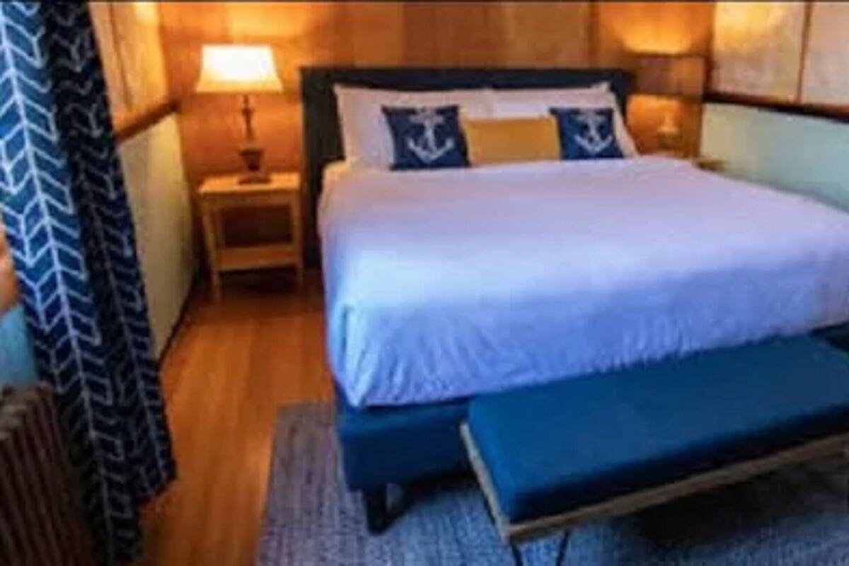 A neatly made bed with a white duvet and two pillows, a bedside table with a lamp, and a bench at the foot of the bed.