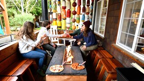 A wooden bench seating area with pizza on a table. - Anchor Inn Resort (Lincoln City)