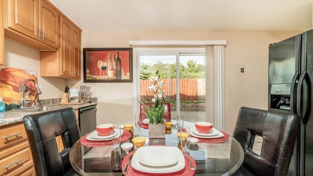 Une cuisine moderne avec un coin repas, comprenant une table ronde en verre, des sets de table rouges et une vue sur le jardin à travers une porte-fenêtre coulissante.