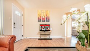 Un salon avec un fauteuil en cuir, un téléviseur à écran plat posé sur un meuble, un plancher en bois et une porte.