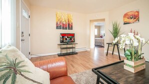 Un salon avec un canapé en cuir, une table basse, un téléviseur posé sur un meuble et un tableau accroché au mur.