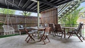 An outdoor patio with a wooden table and chairs, a hanging macrame chair, and a bamboo fence. - 1-17 Heath Street - Stylish Unit on Heath Street (EVANS HEAD)