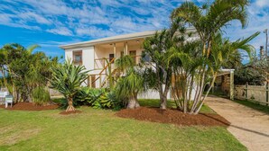 A two-story house with a covered porch, surrounded by a variety of tropical plants and a fenced yard. - 1-17 Heath Street - Stylish Unit on Heath Street (EVANS HEAD)