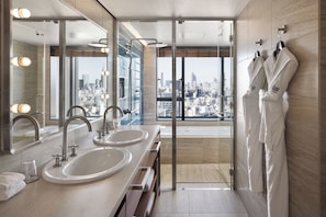 A modern bathroom with dual sinks, a large mirror, and a view of a cityscape through a glass door.