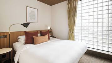 A hotel room with a bed, bedside table, lamp, and window with curtains.
