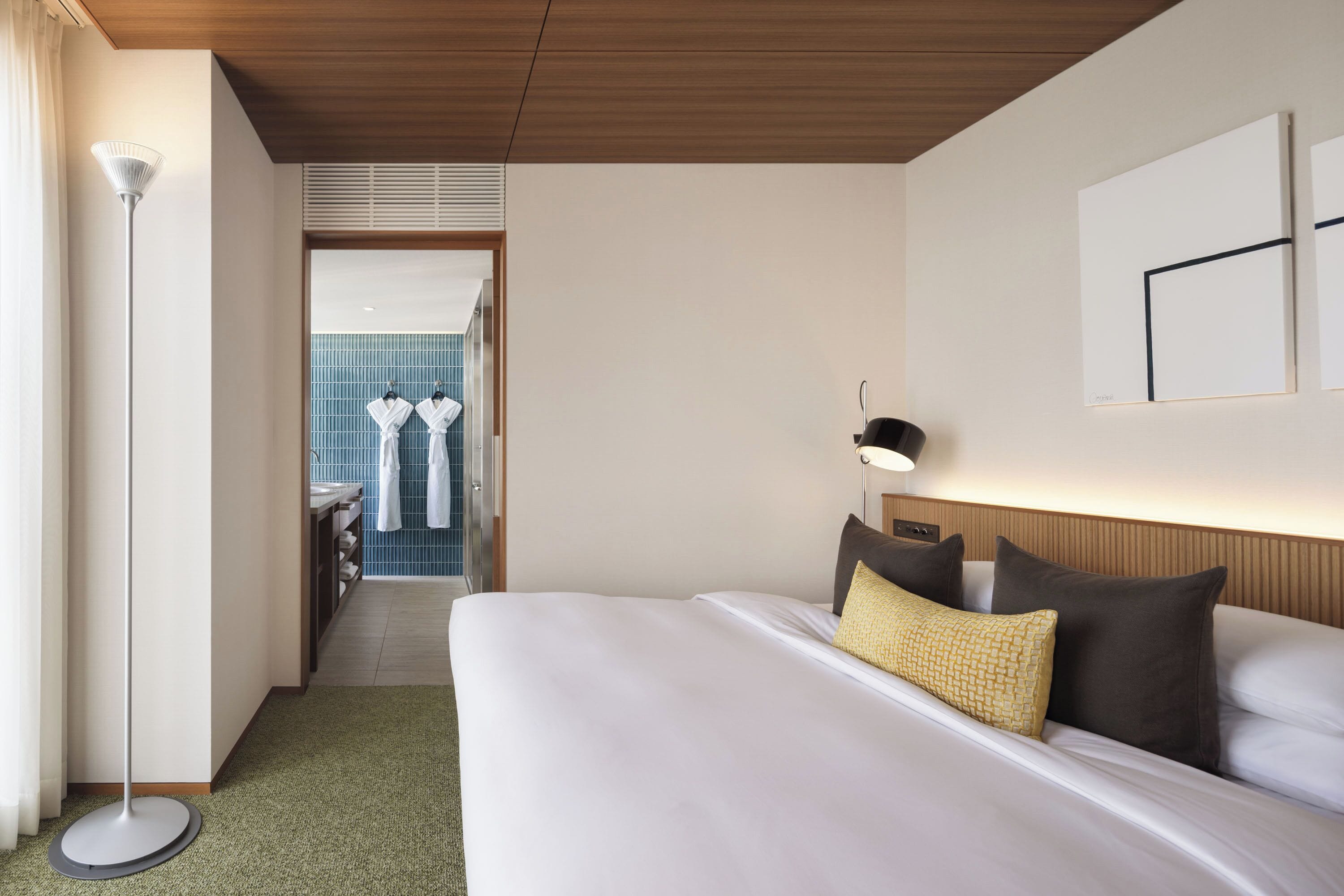 Une chambre d’hôtel avec un lit, une lampe de chevet, un applique murale et une vue sur la salle de bain.