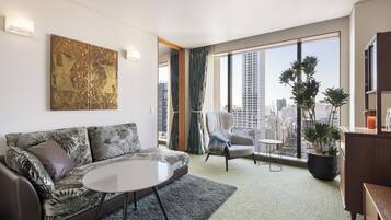 A modern living room with a sofa, armchair, round table, and a large window with a city view.