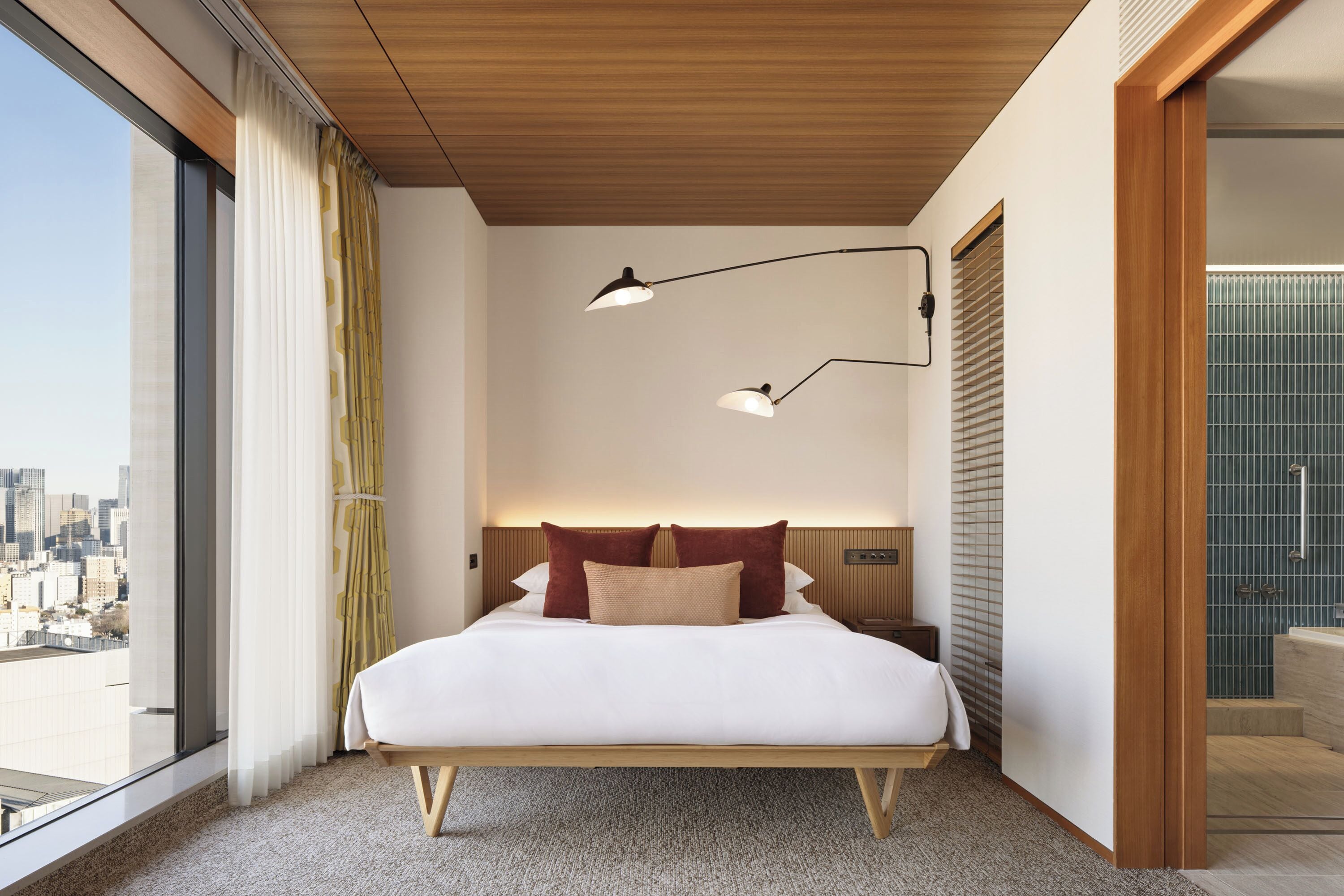 Een moderne hotelkamer met een groot bed, twee bedlampen, uitzicht op de stad en een houten plafond.