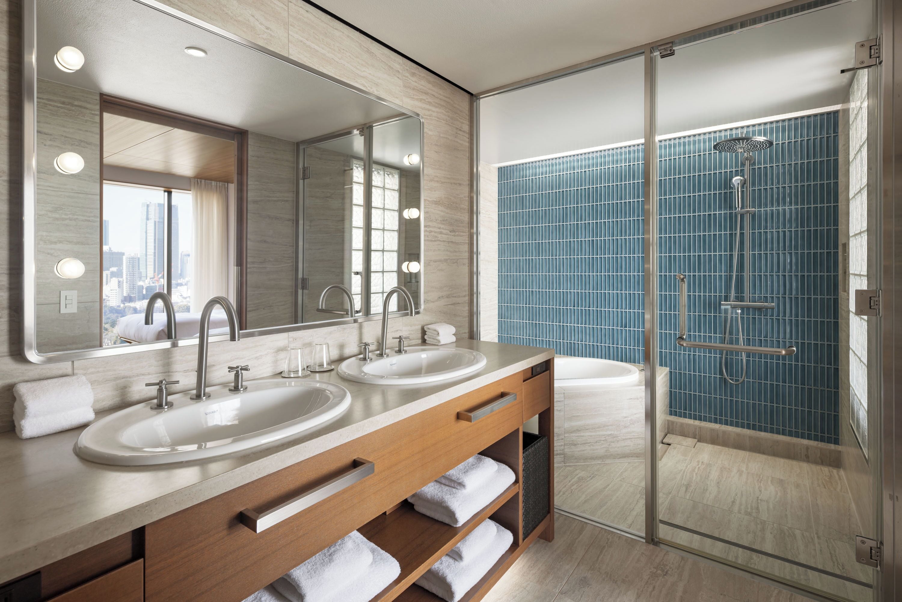 Un baño moderno con dos lavamanos, un espejo grande y una ducha con mampara de vidrio.