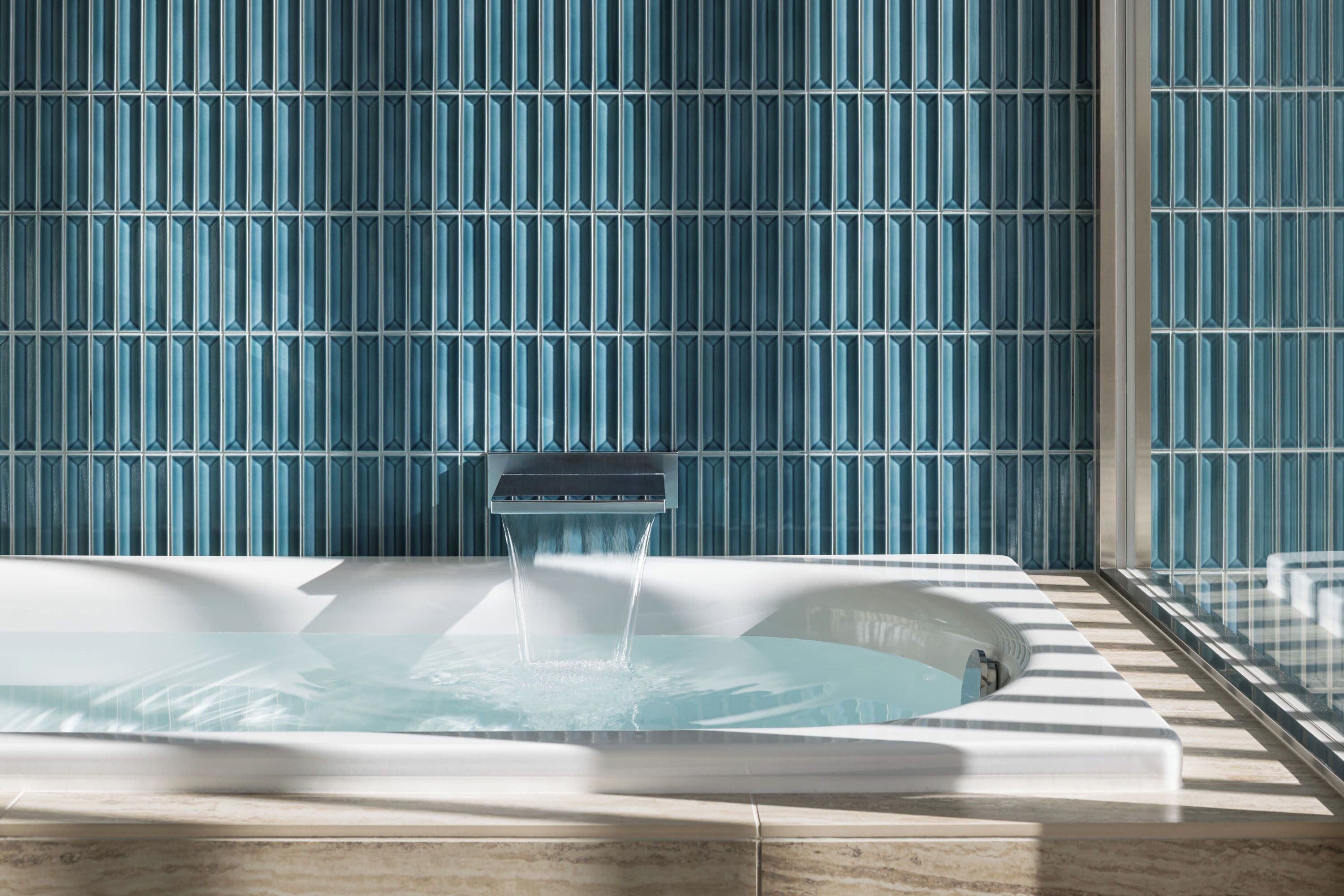 A hot tub with water flowing, set against a wall with a blue pattern.