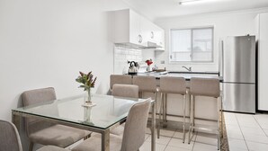 A modern kitchen with white cabinetry, a stainless steel refrigerator, and a glass dining table with four chairs. - 1-68 Woodburn Street (EVANS HEAD)