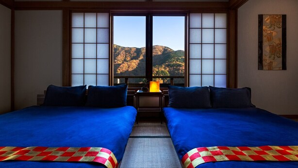 A traditional Japanese-style room with two beds, a view of mountains, and a painting on the wall. - Taisho modern Villa ZEN (Hakone)