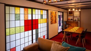A room with a wooden dining table, chairs, a sofa, and a wall with colorful stained glass panels. - Taisho modern Villa ZEN (Hakone)