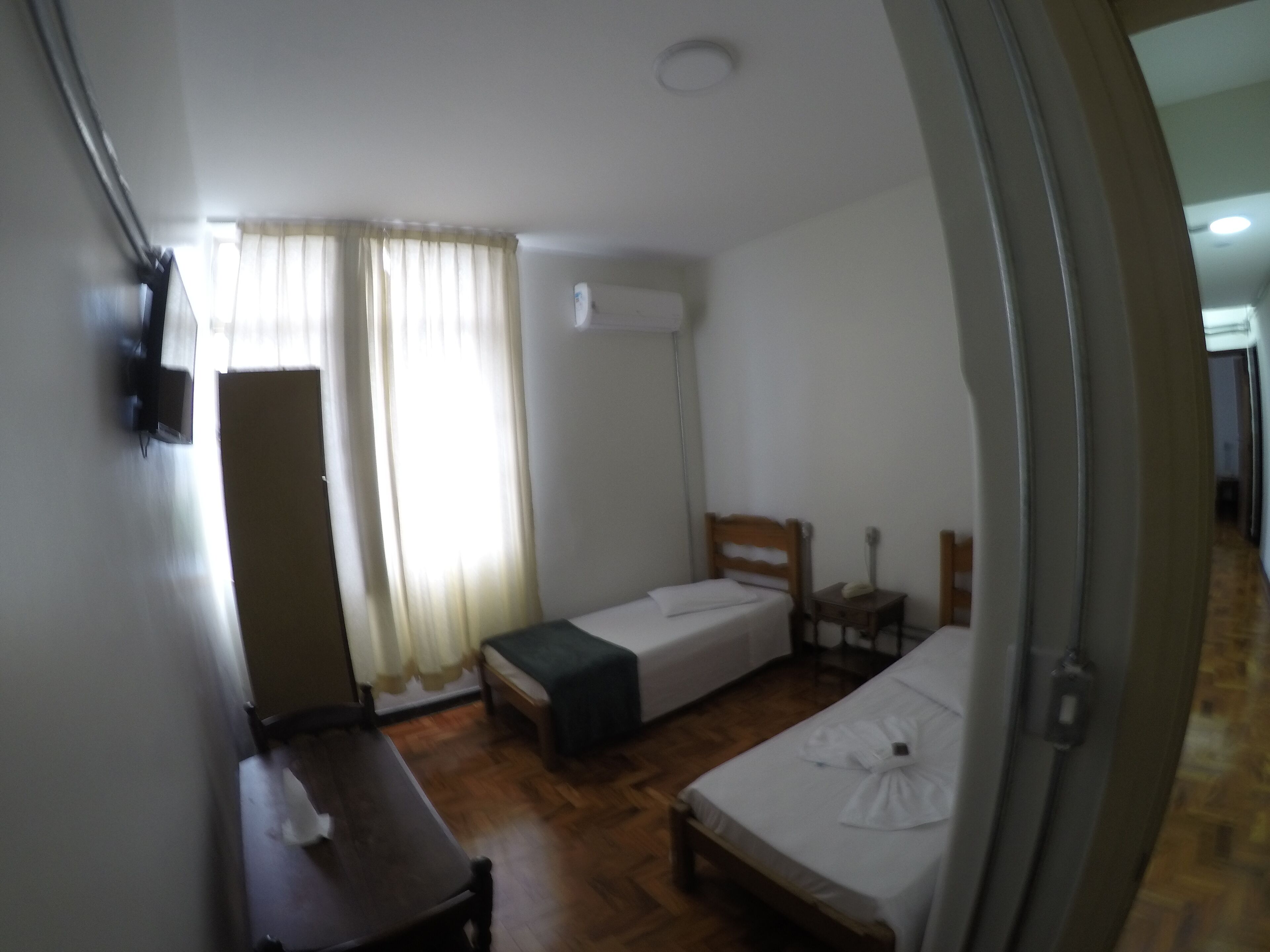 Una habitación pequeña y limpia con dos camas individuales, una mesa de madera, un escritorio y una silla.