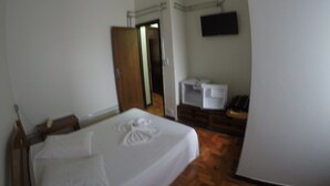 Un dormitorio con una cama, un armario de madera, un televisor en la pared y un mueble blanco pequeño.