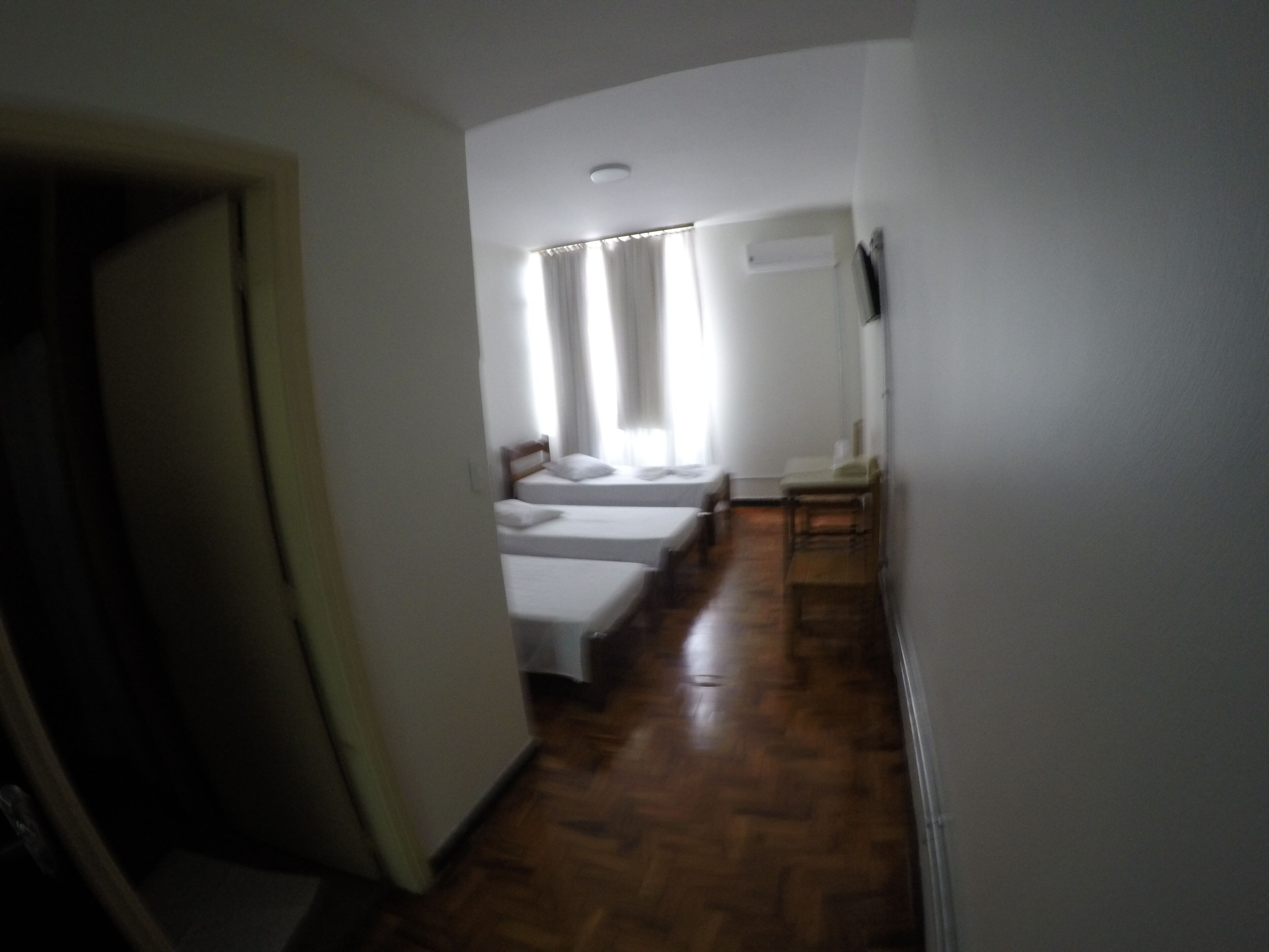Un pasillo estrecho con piso de madera que conduce a una habitación con dos camas y una silla.