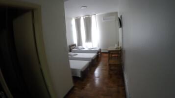 Un pasillo estrecho con piso de madera que conduce a una habitación con dos camas y una silla.