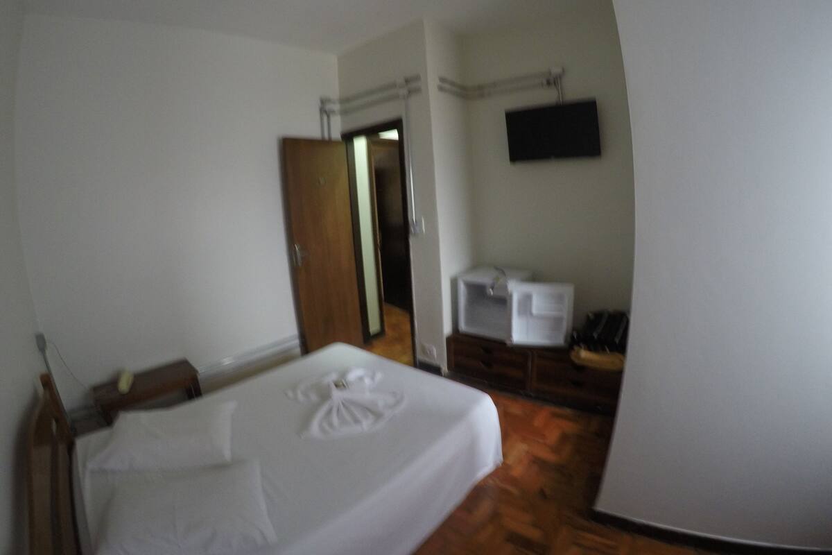 A bedroom with a bed, a wardrobe, a television, and a small kitchenette area.