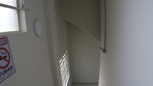 Una escalera estrecha con barandilla, un letrero de prohibido fumar y una ventana a la izquierda.