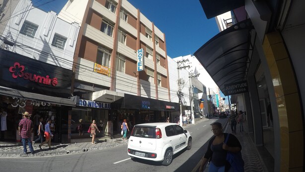 Vista de la calle con un cartel de hotel, comercios y peatones.