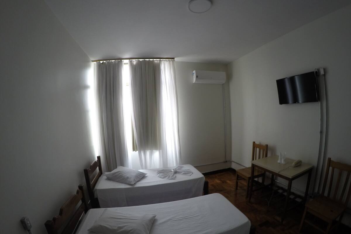 A hotel room with two single beds, a desk, a chair, and a flat-screen TV mounted on the wall.