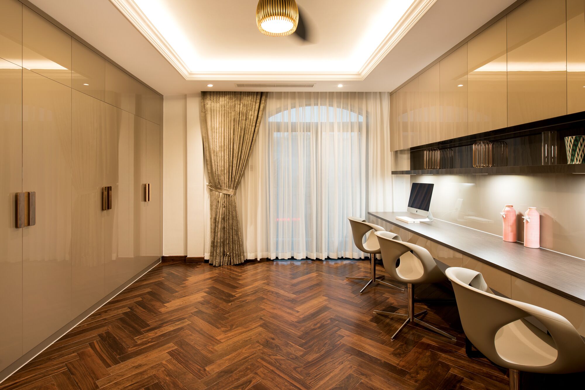 Une cuisine moderne avec un parquet en bois disposé en chevrons, un îlot central intégré avec des tabourets de bar et une grande fenêtre agrémentée de rideaux légers.
