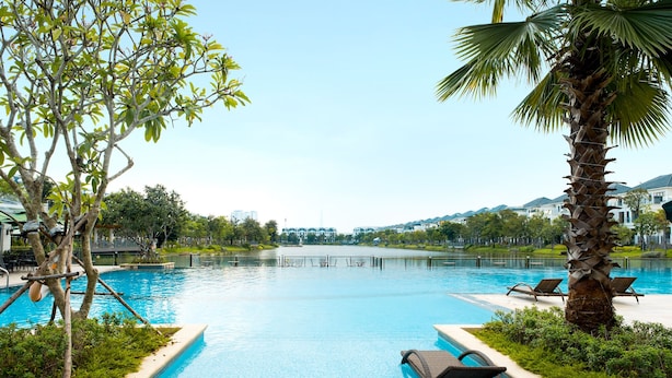 Una piscina con sillones de descanso, rodeada de follaje y vistas a edificios al fondo.