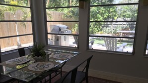 Comedor con mesa de vidrio, sillas y vista a un patio trasero con una parrilla.