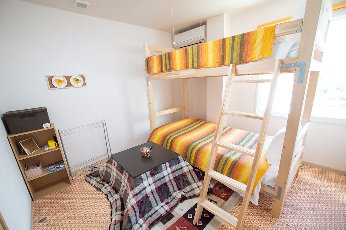 A bunk bed room with a small table and a shelf unit.