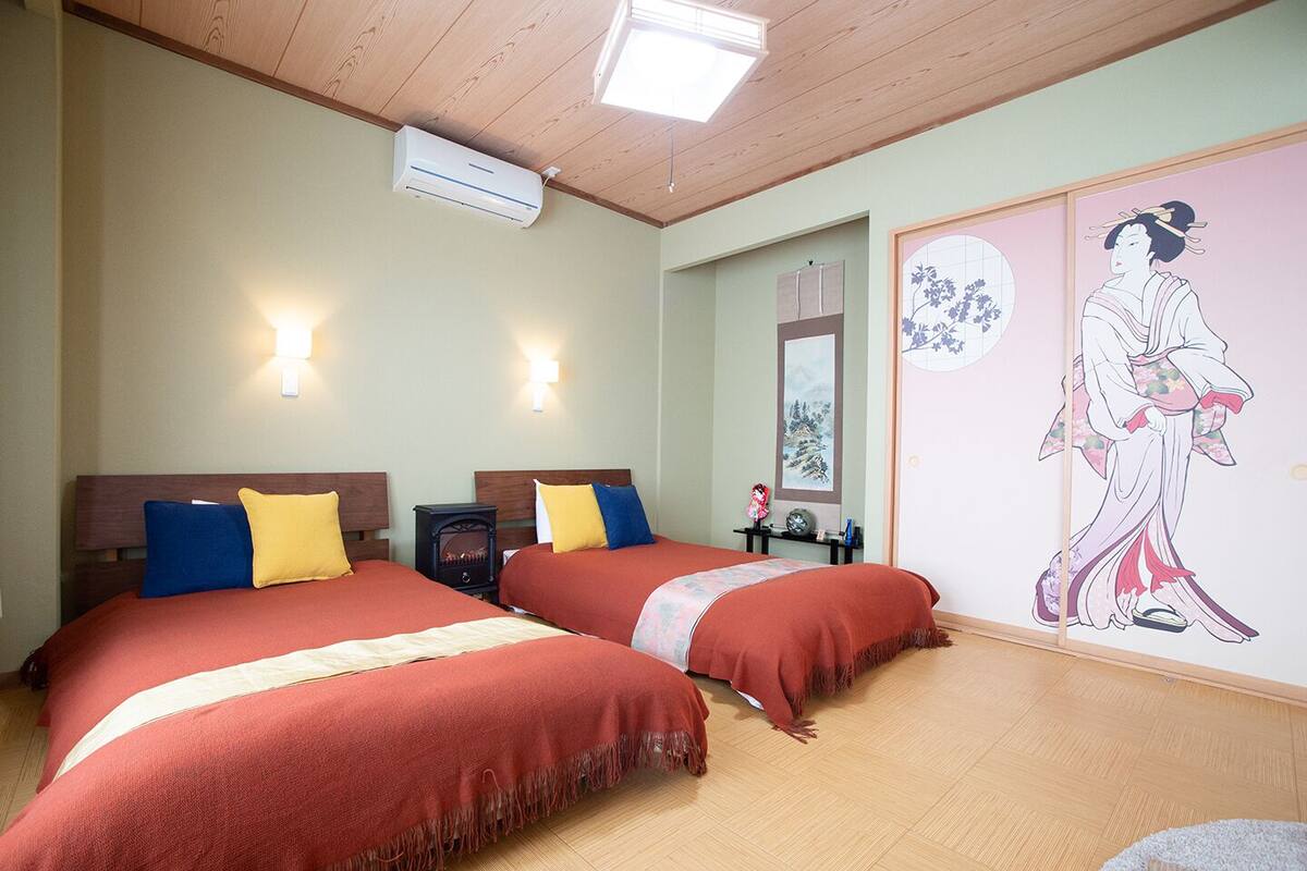 A hotel room with two beds, a heater, wall-mounted air conditioning, and traditional artwork.