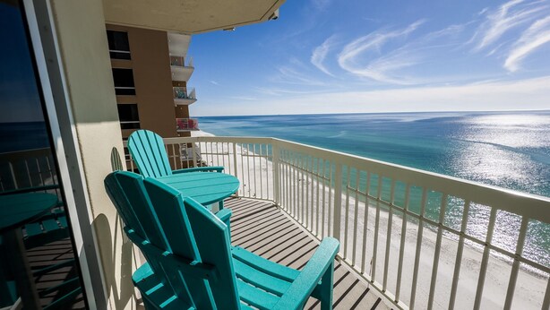 A balcony with turquoise chairs and a table, overlooking a beach with clear blue water and a white railing. - Labor Day special at Celadon 1201: 3 bed/3 bath beachfront (Panama City Beach)