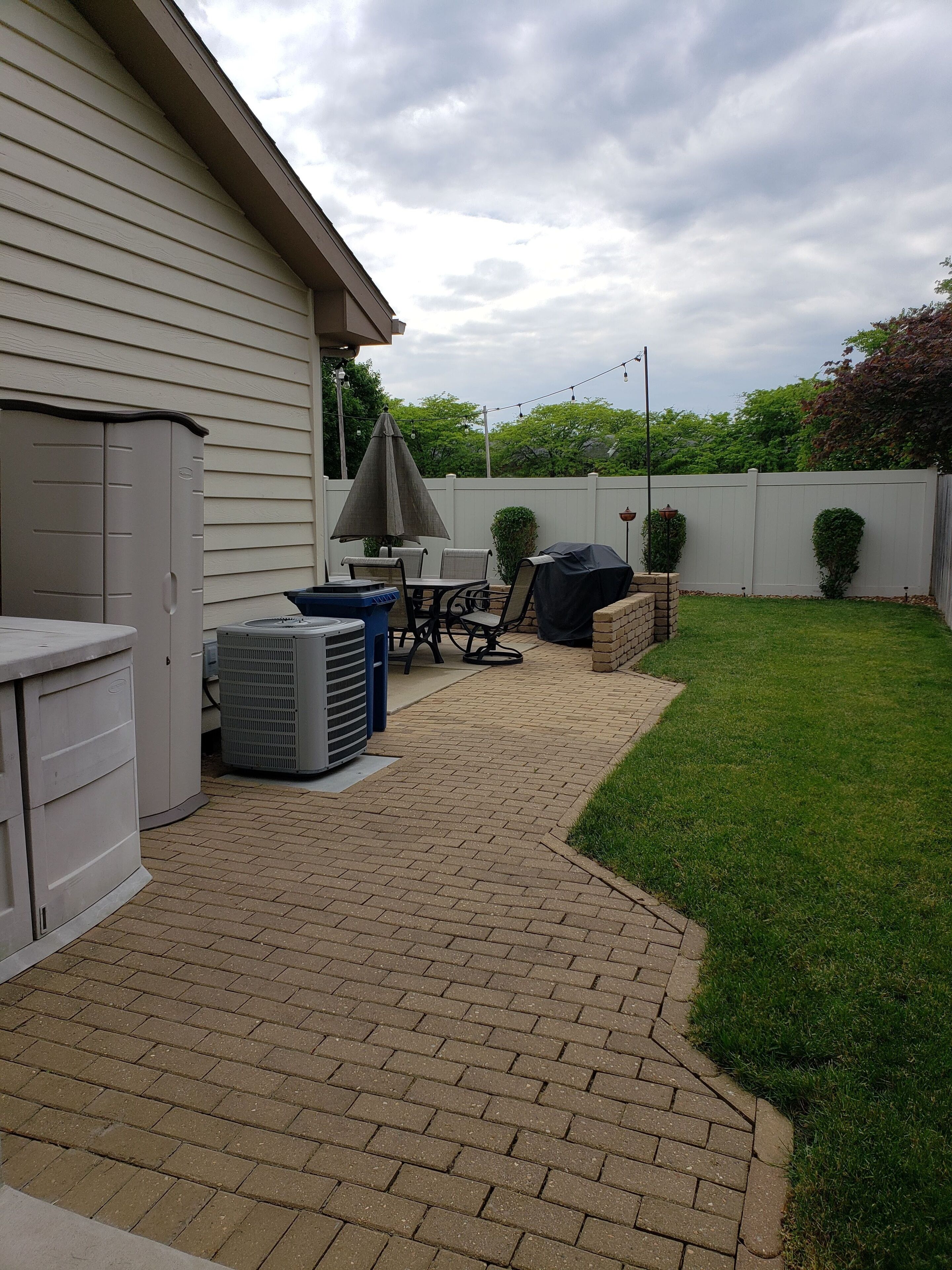 Une terrasse à l’arrière de la maison, avec un barbecue, du mobilier d’extérieur et un abri de jardin.