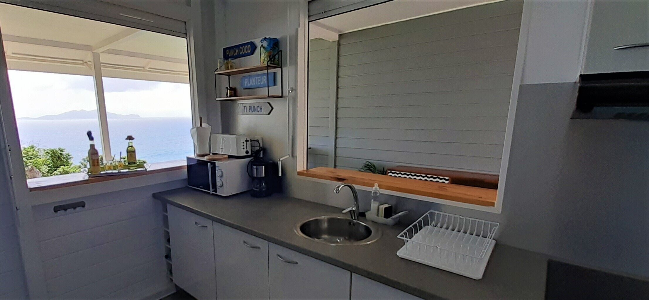 A compact kitchen with a sink, a coffee maker, and a window offering a view of the sea.
