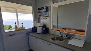 A compact kitchen with a sink, a coffee maker, and a window offering a view of the sea. - Magnificent views of the sea and islands of Les Saintes, lulled by the sound of the waves. (Trois Rivieres)