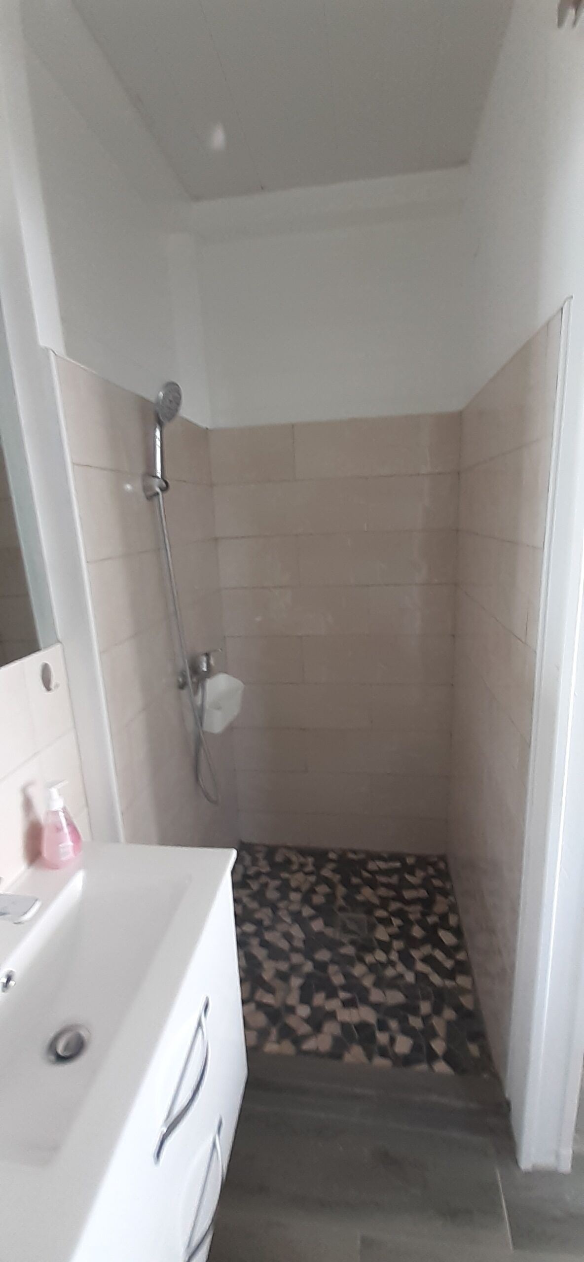 A small bathroom with a shower, a white sink, and patterned floor tiles.