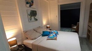 A bedroom with a bed, two bedside tables, a nightstand, a chair, and a door leading to a balcony. - Magnificent views of the sea and islands of Les Saintes, lulled by the sound of the waves. (Trois Rivieres)