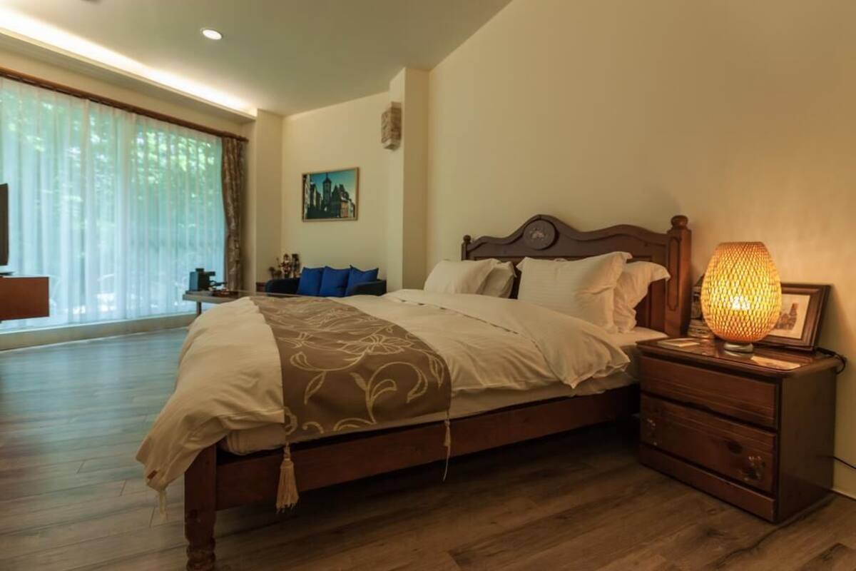 A bedroom with a wooden bed, a nightstand with a lamp, and a painting on the wall.