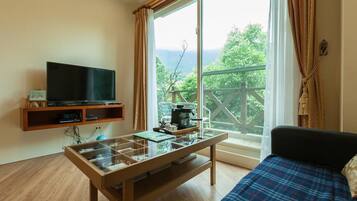 A room with a bed, a TV on a shelf, a coffee machine, and a table with a glass top.